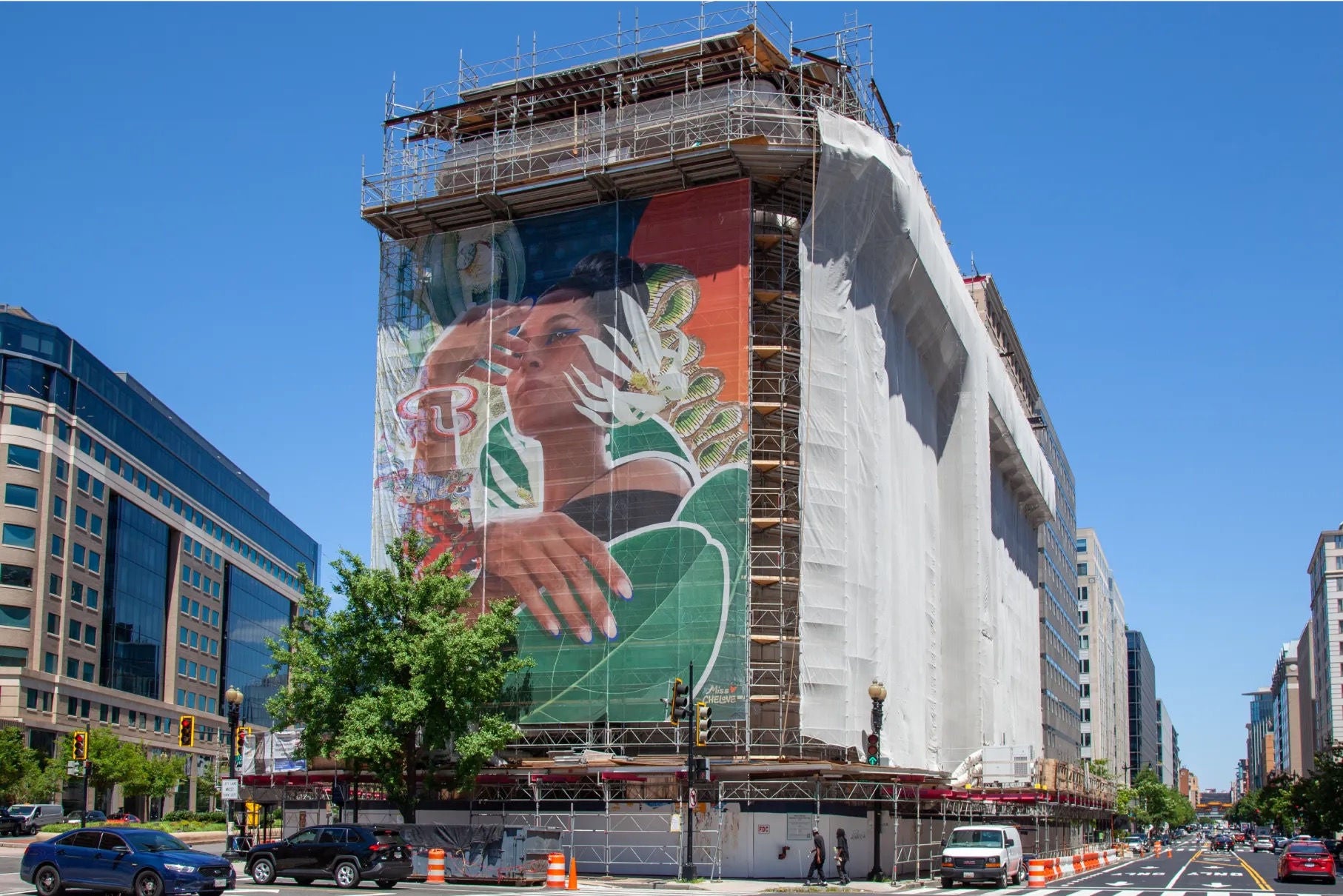 A building covered in scaffolding on three sides, with the fourth side showing a large mural 