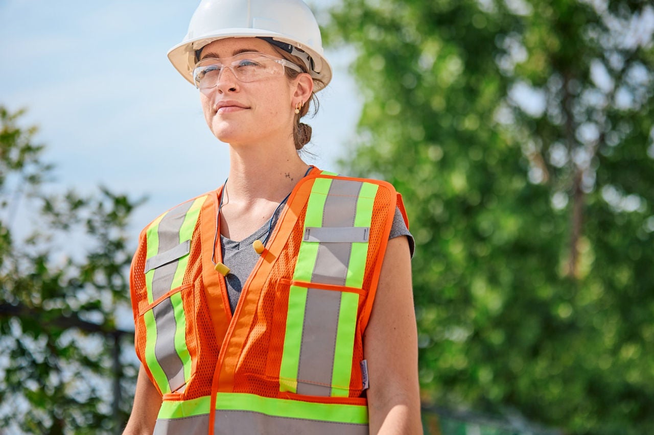 Woman in safety gear and hard hat standing outdoors at a construction site