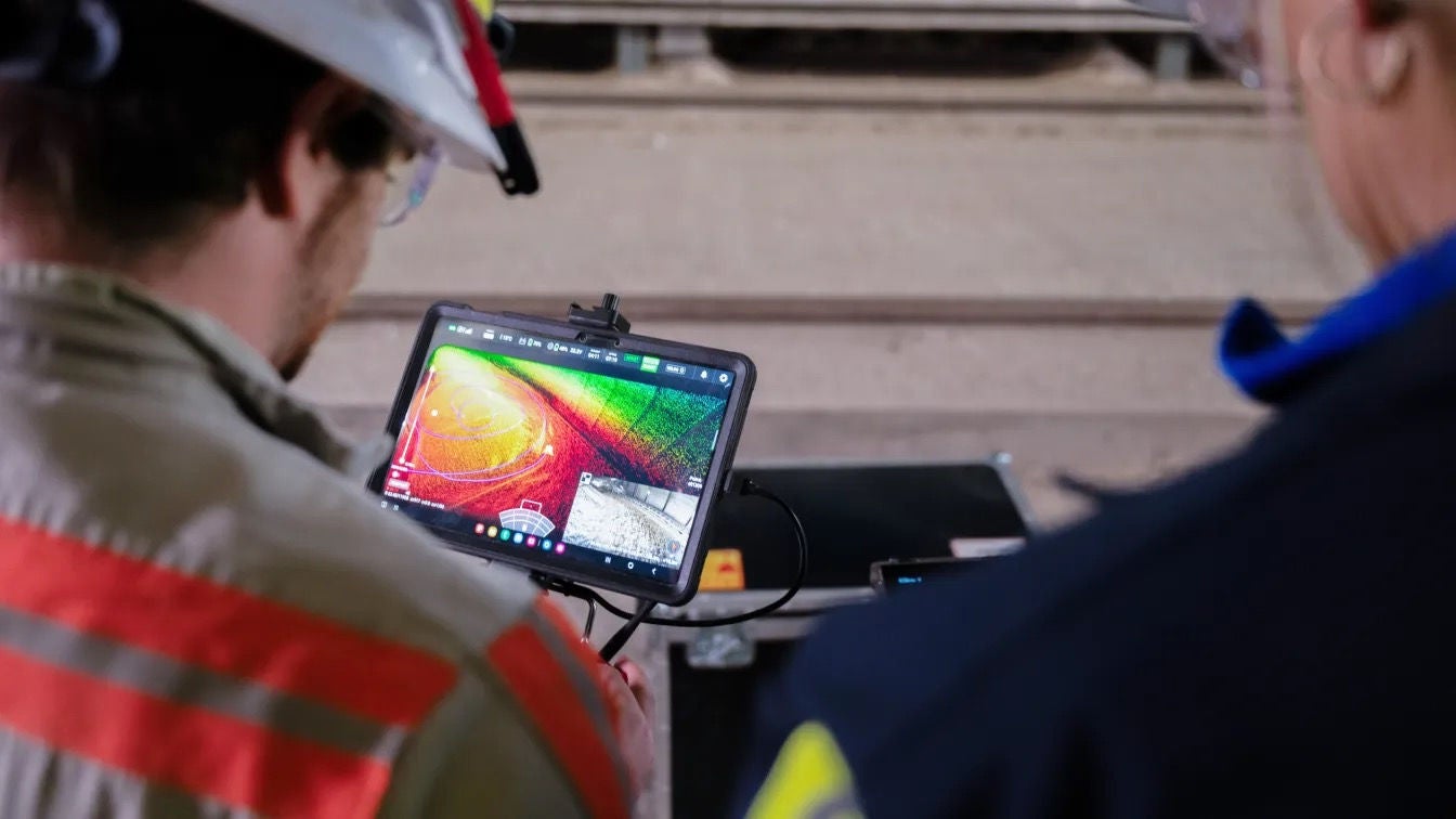 Two workers looking at a screen that’s displaying an AI-augmented image of concrete 