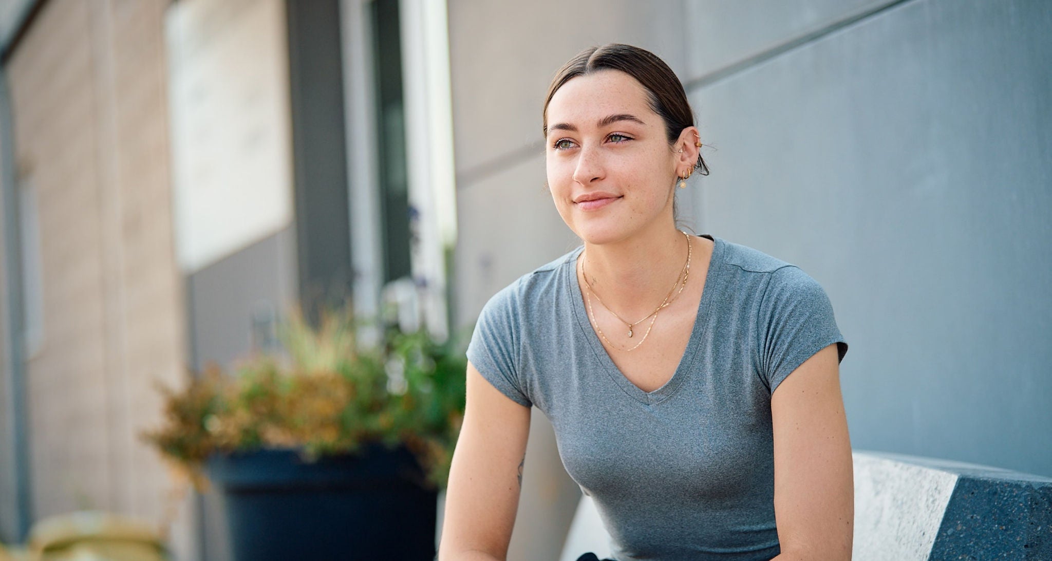 Young woman with a satisfied expression sitting on a bench in from on a commercial building