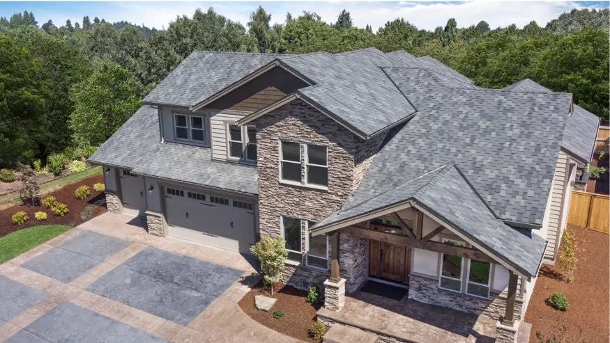 two-story house with a light gray roof, stone facade, and a three-car garage