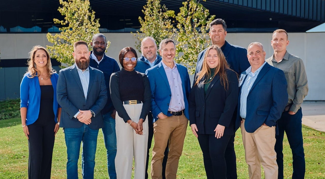 A group of professionals in business casual attire posing for a group photo in front of a commercial facility