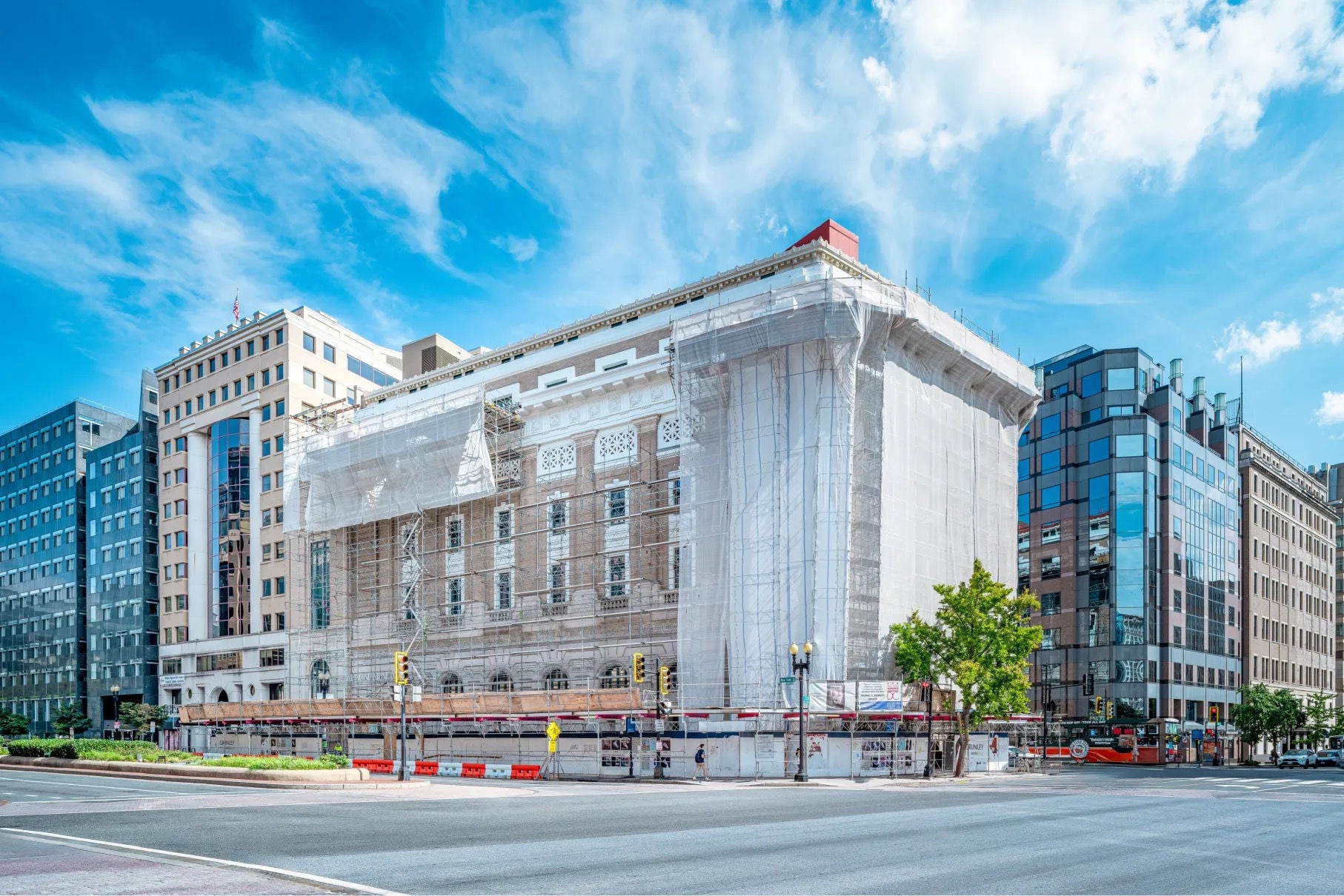 In a city, a large building partly covered in protecting sheeting and scaffolding