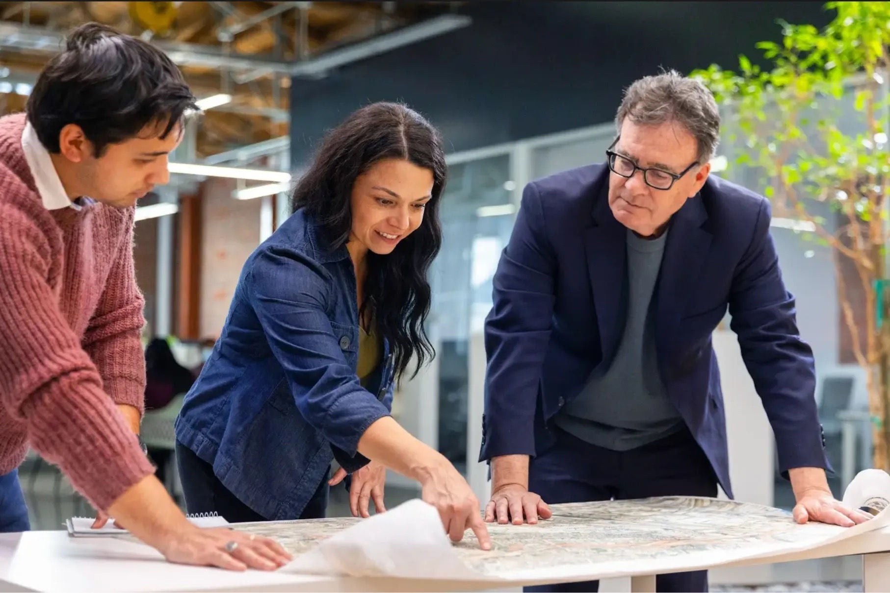 Three professionals collaborating in an office, reviewing building plans together