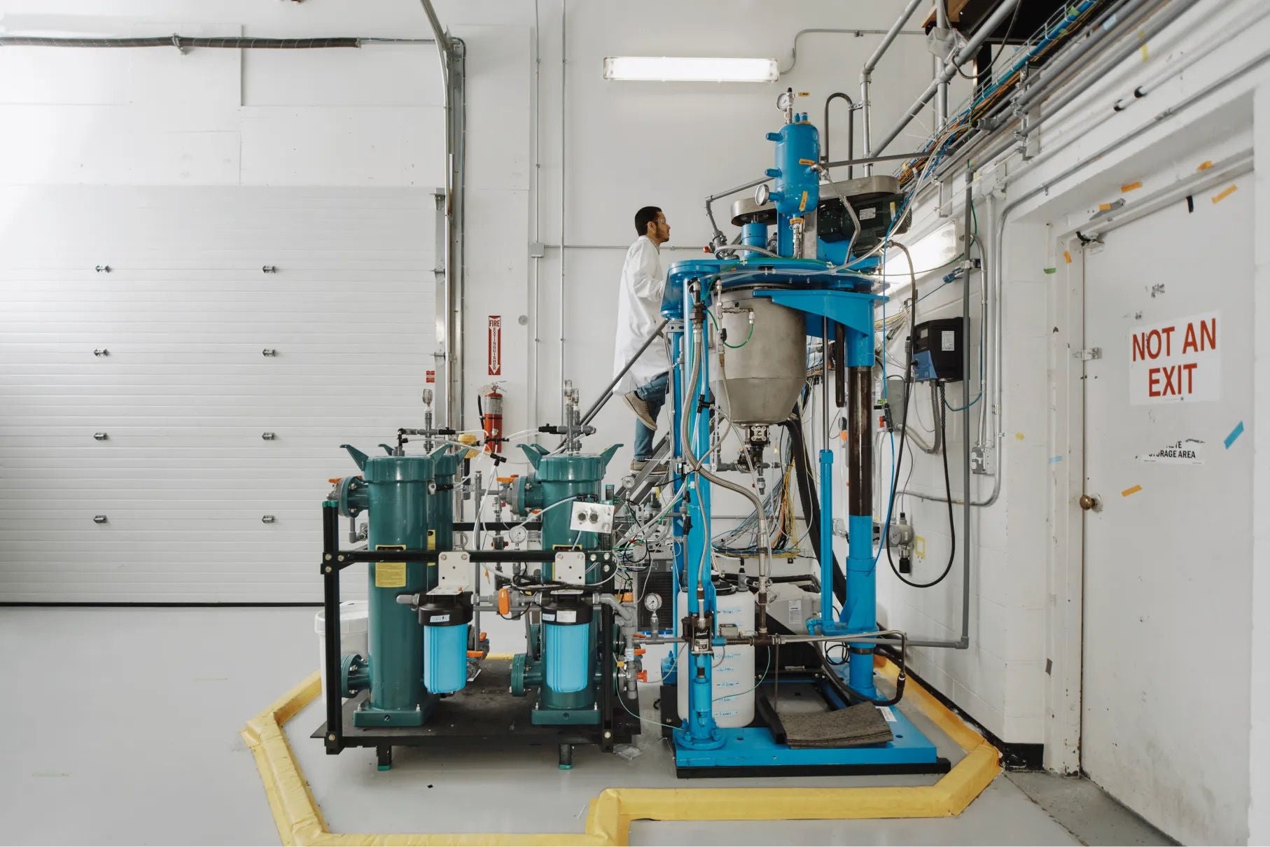 A man in a lab coat ascends a ladder beside a large piece of industrial equipment