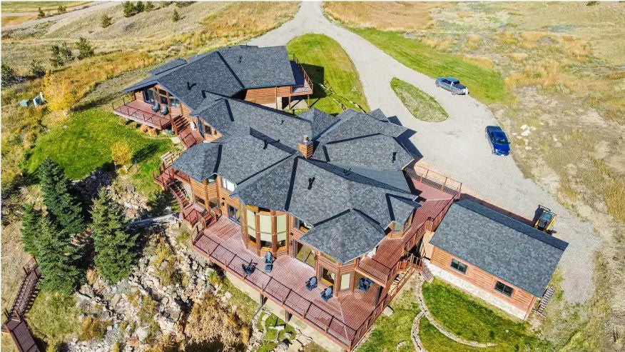 Large rural estate, wooden exterior, gray roof, and a winding driveway