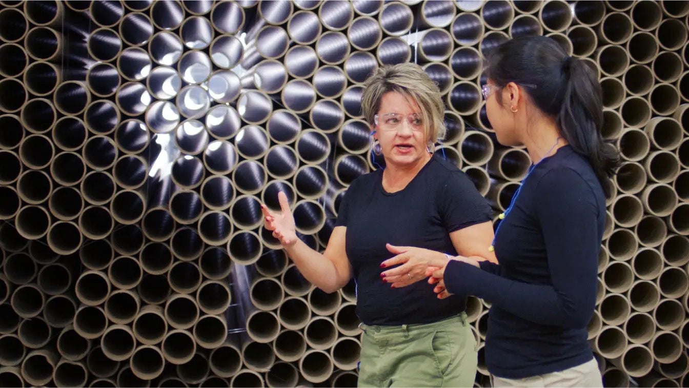Two woman talking in front of a pile of stacked metal tubing
