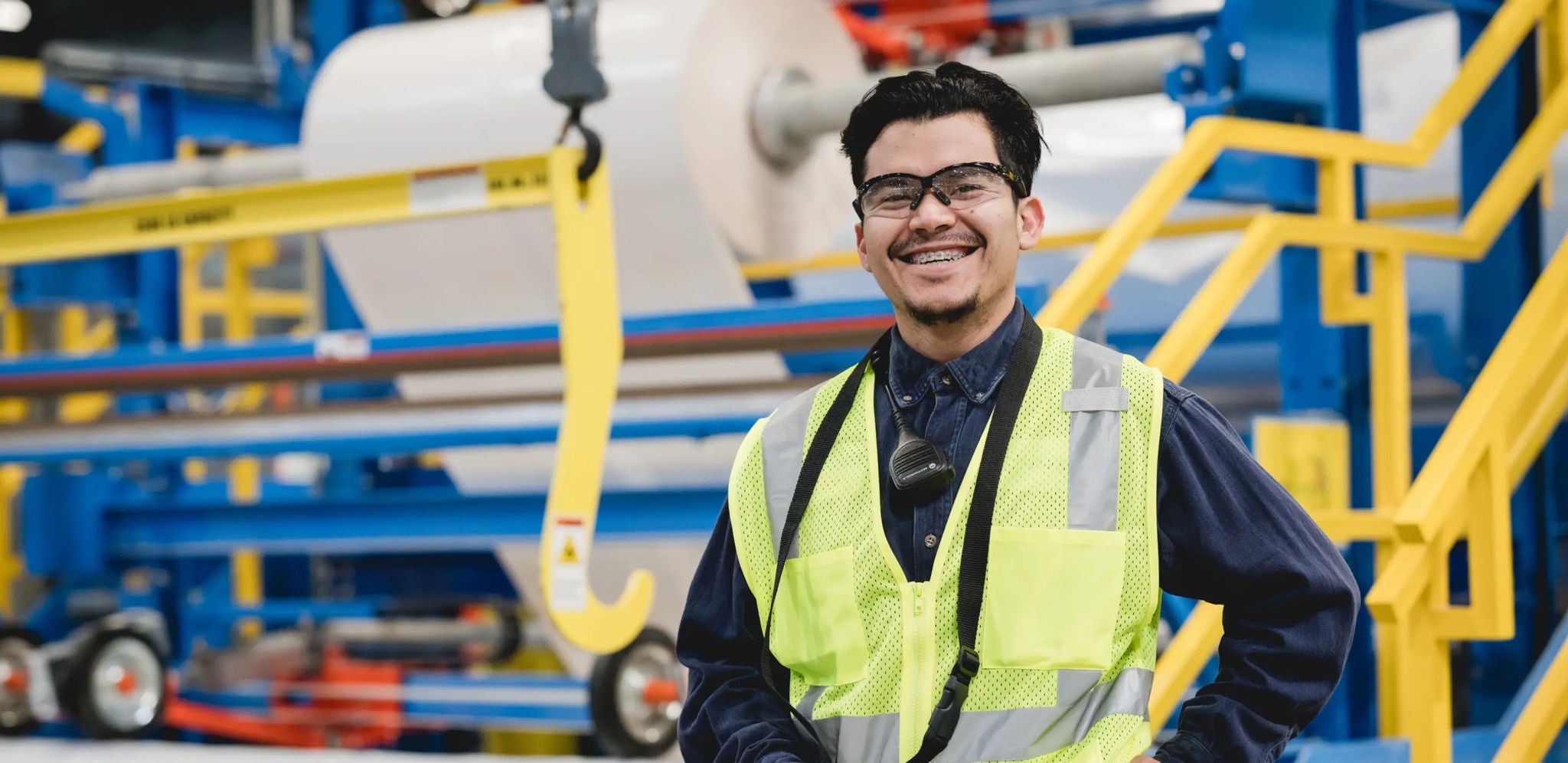 A worker wearing a safety vest standing in front of a large industrial machine