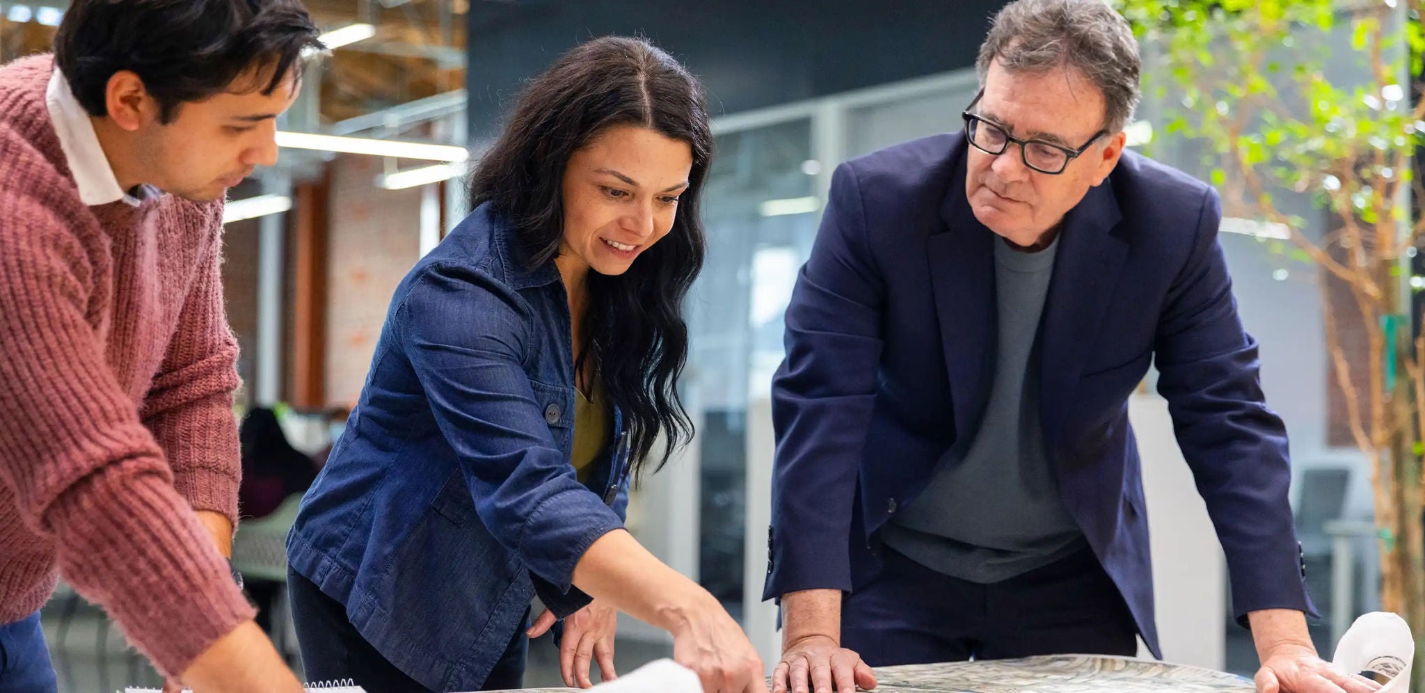 Three professionals collaborating in an office, reviewing building plans together