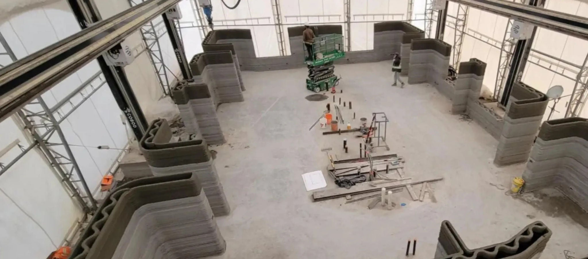  Overhead view of 3D-printed building site with curved walls and workers operating machinery