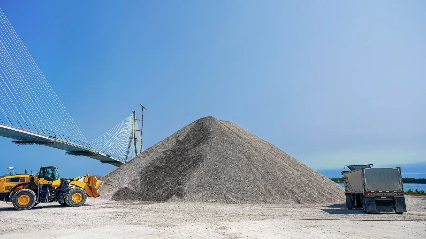 Pile de granulat, camions de construction, pont Gordie Howe en arrière-plan 
