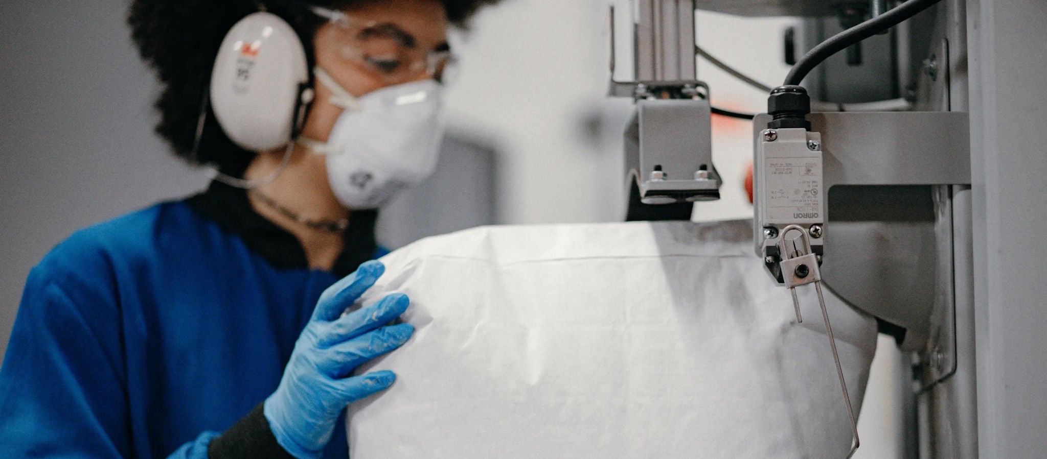  A worker holding a large bag of cement that’s being sealed by a machine